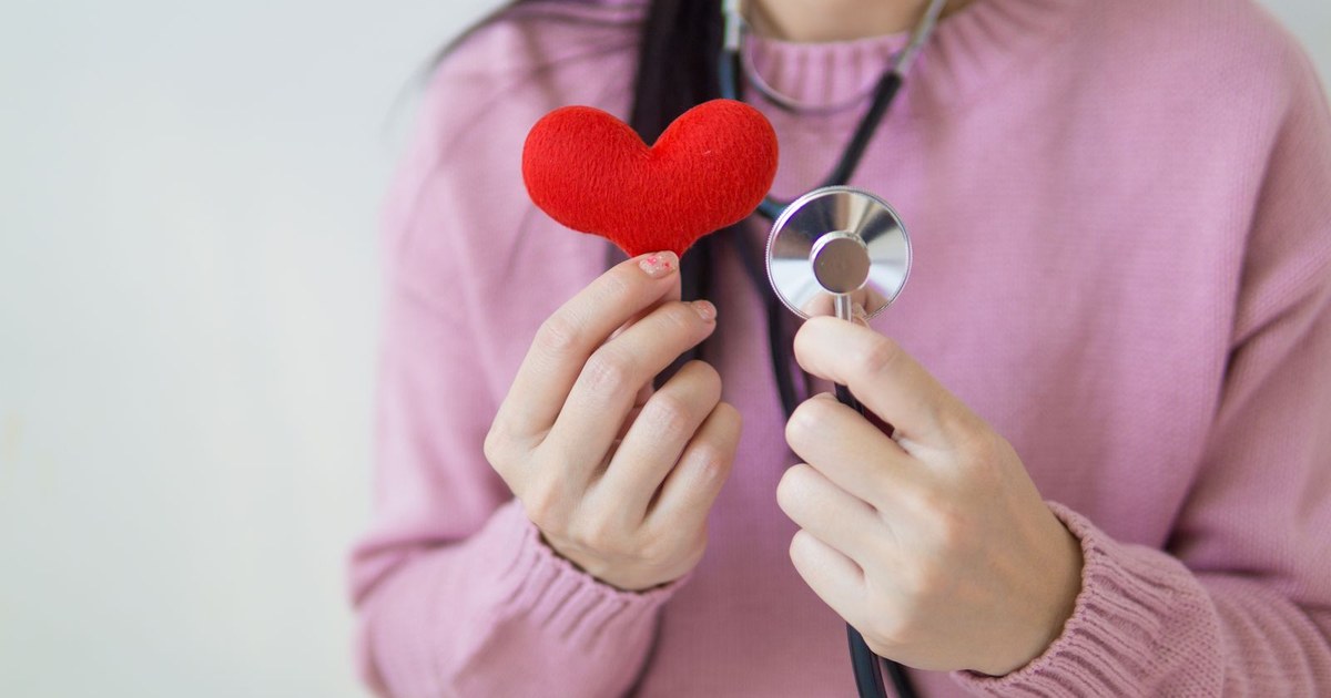 A woman in a pink sweater holding a small red heart and a stethoscope