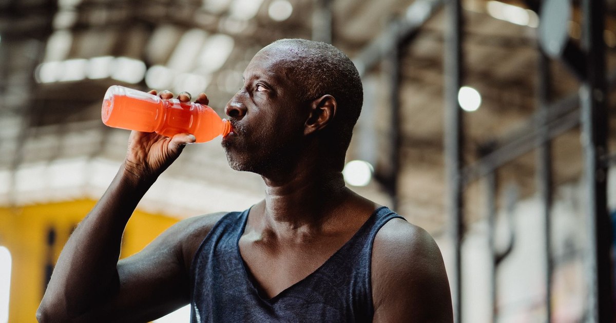 A man drinking an orange electrolyte sports drink from a bottle after a workout
