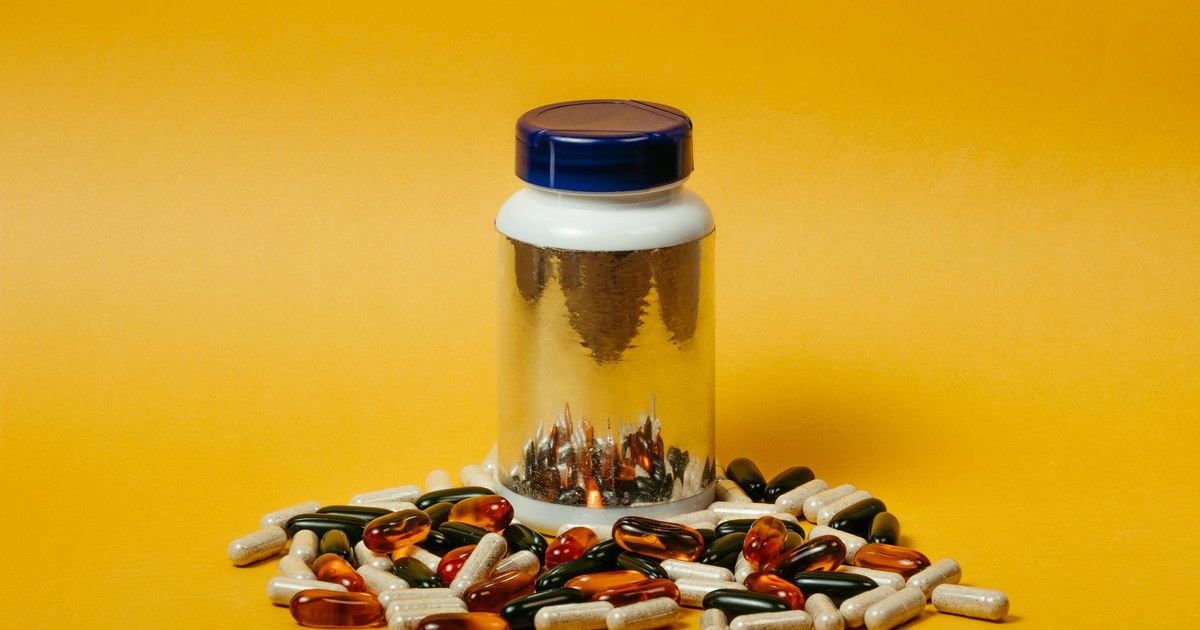 A supplement bottle surrounded by assorted colorful capsules on a yellow background