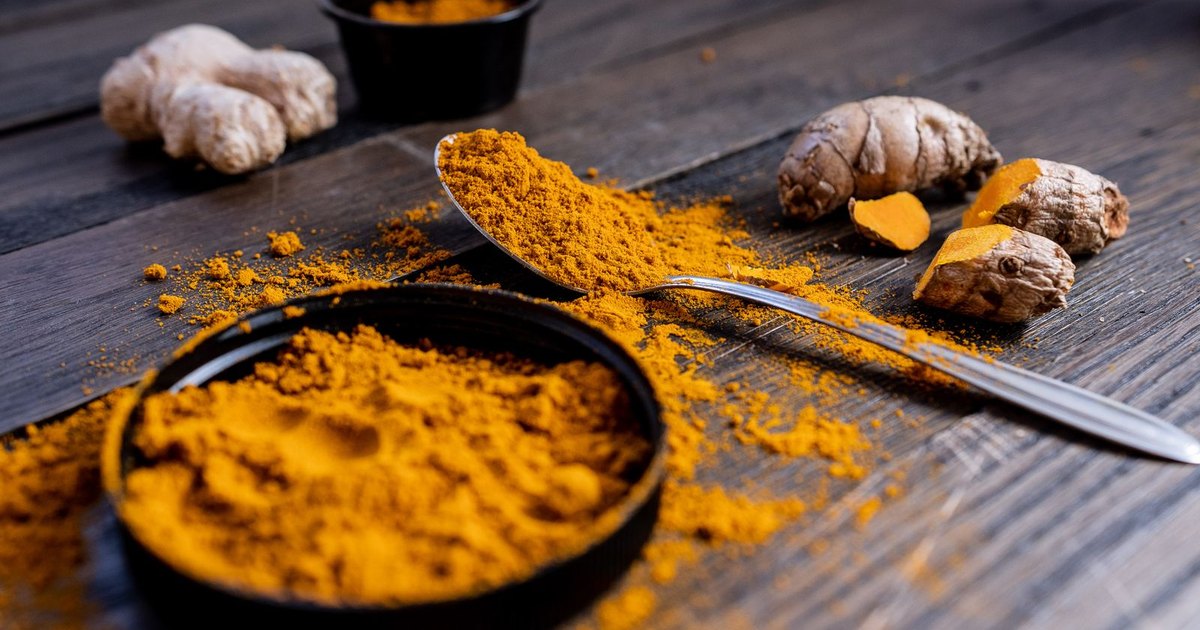 Fresh turmeric and ginger root with a spoon of golden turmeric powder on a dark wooden table