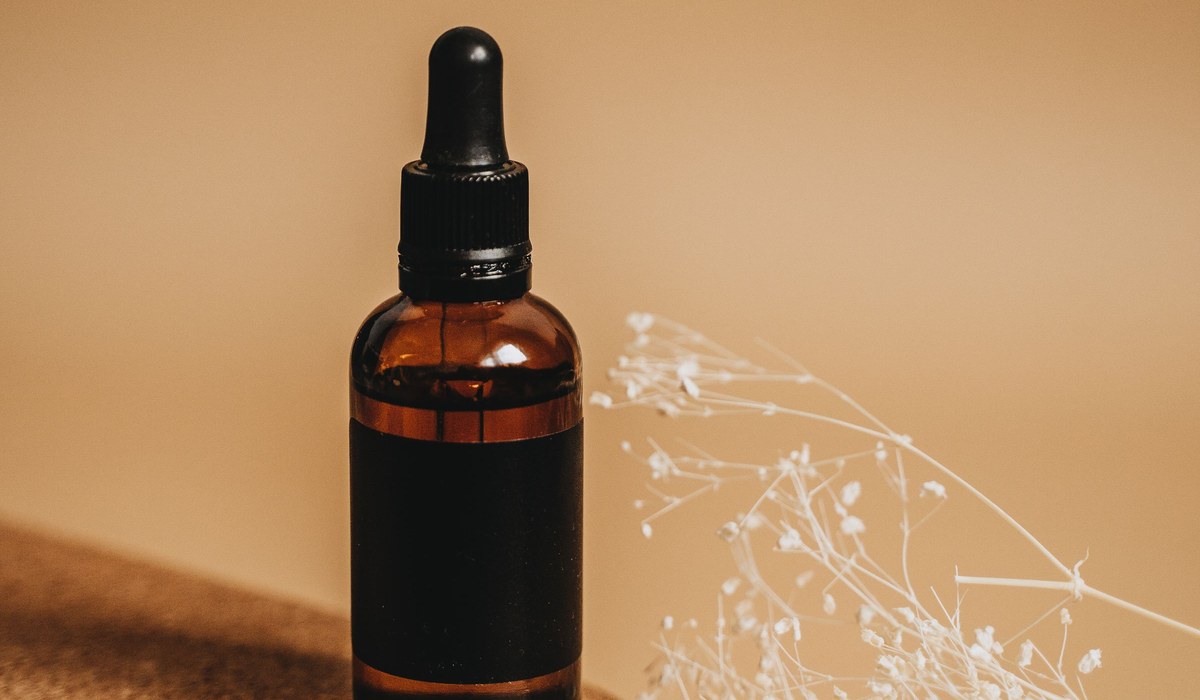 An amber glass dropper bottle of black seed oil on a cork coaster