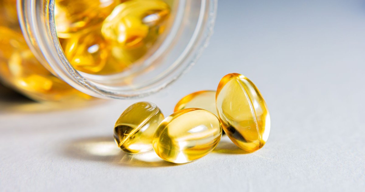 Amber-gold softgel capsules spilling from a glass jar onto a white surface, the form CoQ10 is usually sold in