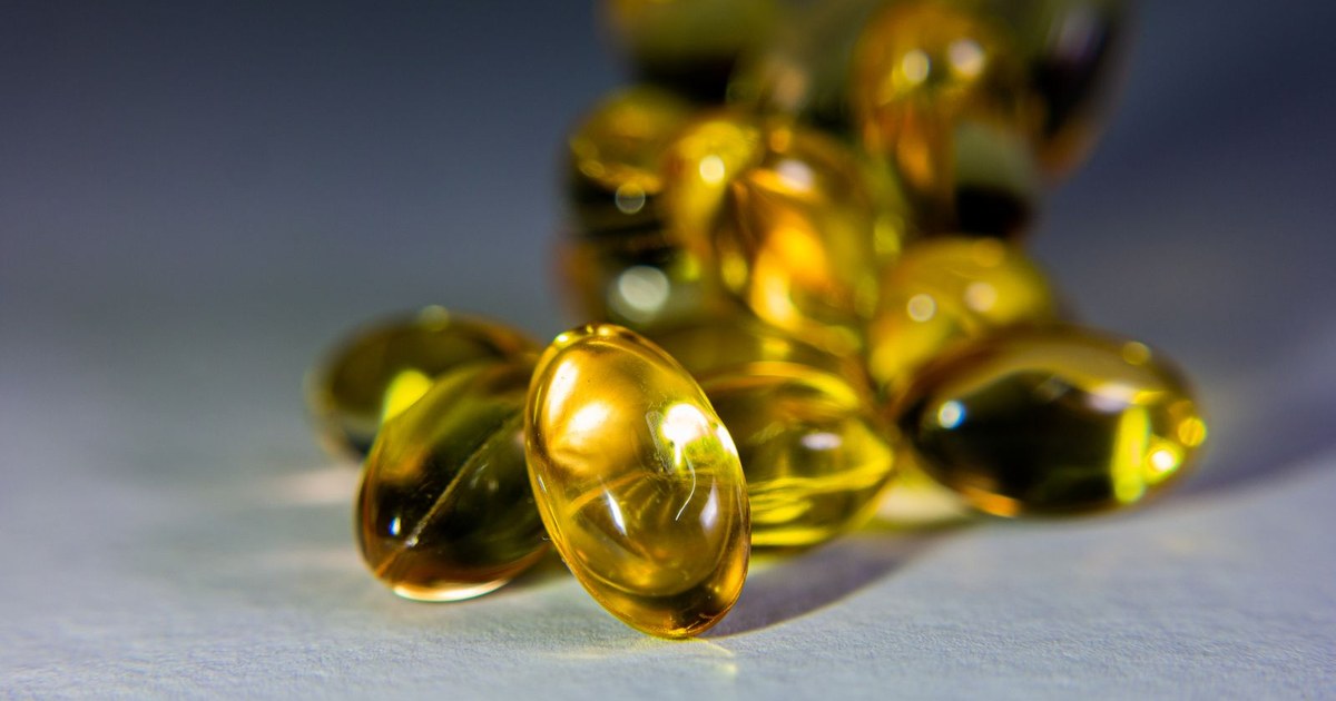 Golden amber translucent softgel capsules spilling onto a pale surface