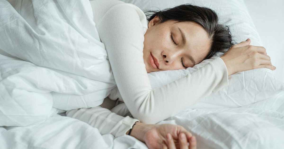 A woman sleeping peacefully in bed under soft white bedding