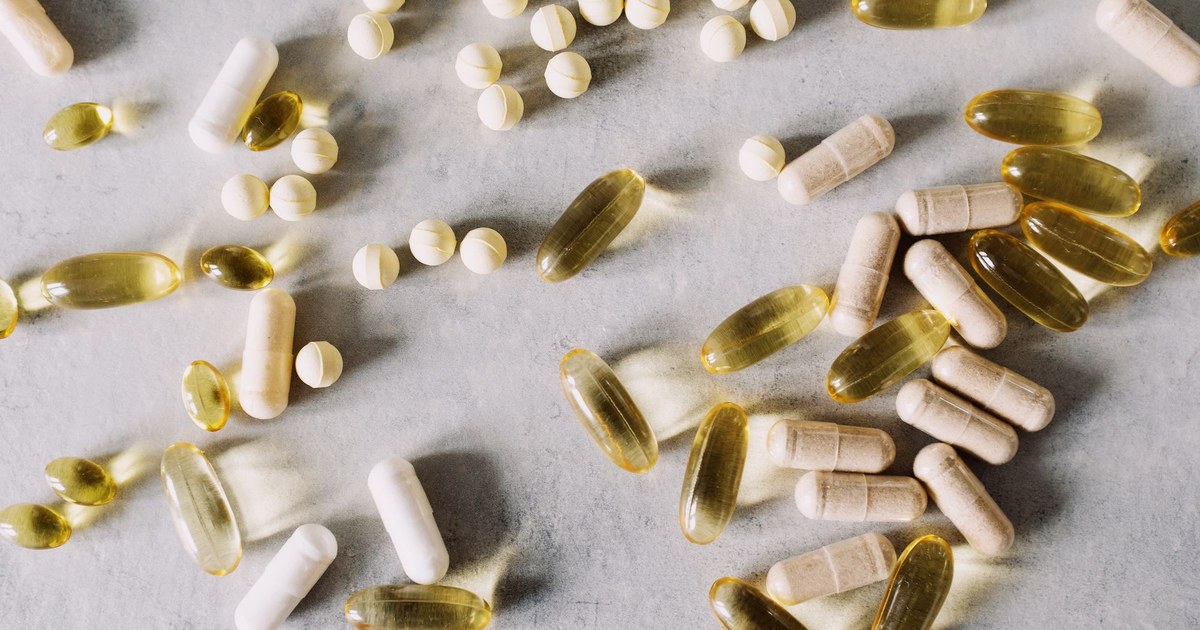 An assortment of vitamin tablets, capsules, and golden softgels on a gray surface