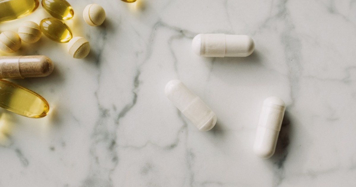 White supplement capsules and amber softgels on a white marble surface