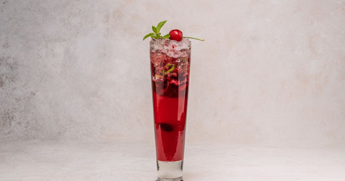 A deep red tart cherry mocktail in a tall glass with mint and a cherry
