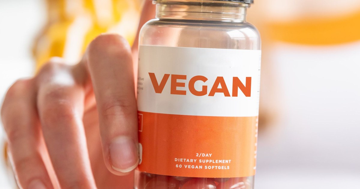A hand holding a supplement bottle and reading the label