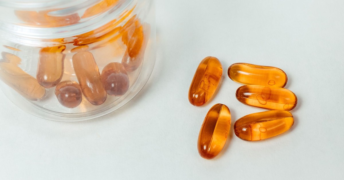 A glass jar of amber supplement capsules spilling onto a white surface