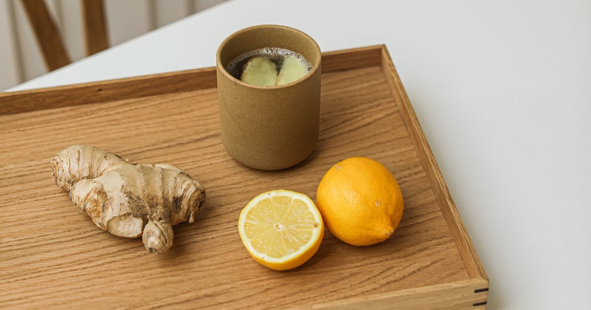 A mug of steaming ginger tea on a wooden tray with fresh ginger root and a halved lemon