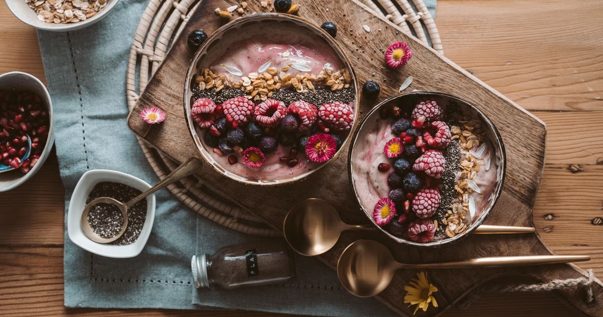Two bowls of berry smoothie topped with granola, chia seeds, and fresh berries on a wooden board
