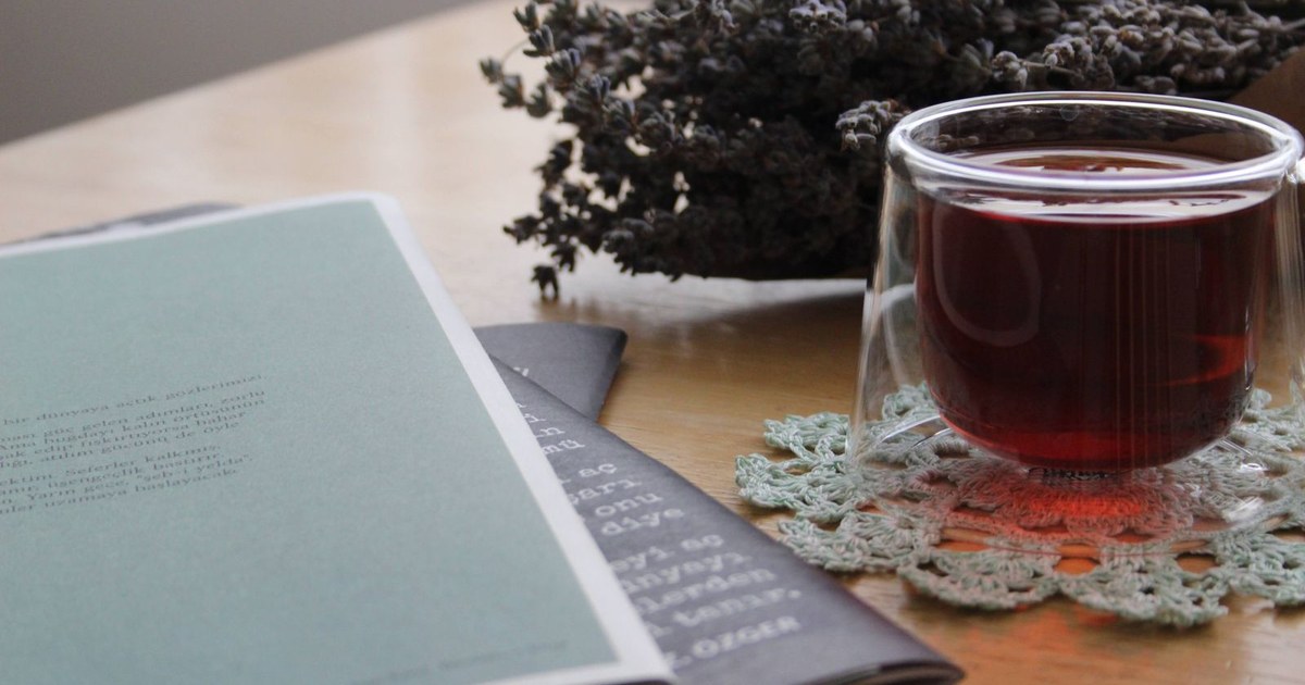 A glass mug of herbal tea beside a sprig of dried lavender and a notebook on a light wooden table