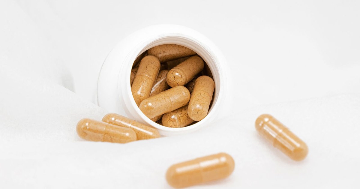 Tan magnesium supplement capsules spilling from a small white jar onto a white cloth