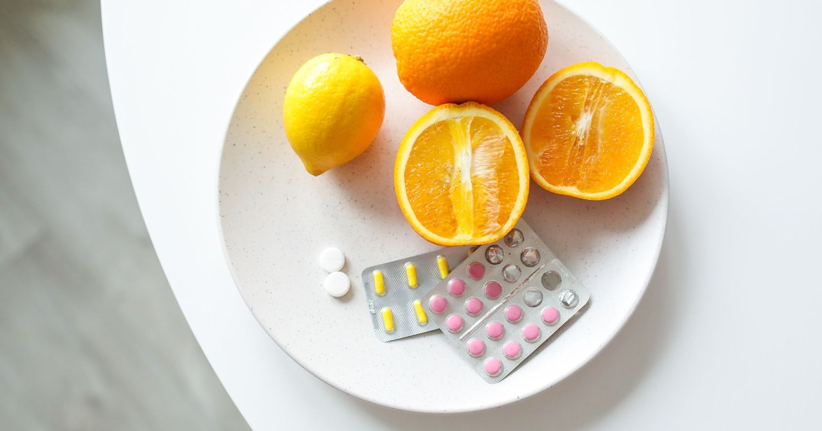 Citrus fruits on a plate beside blister packs of vitamins